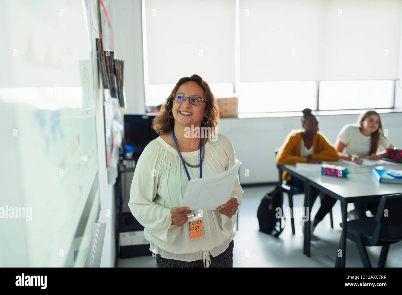 Sorridente insegnante che conduce la lezione sullo schermo di proiezione in classe Foto Stock