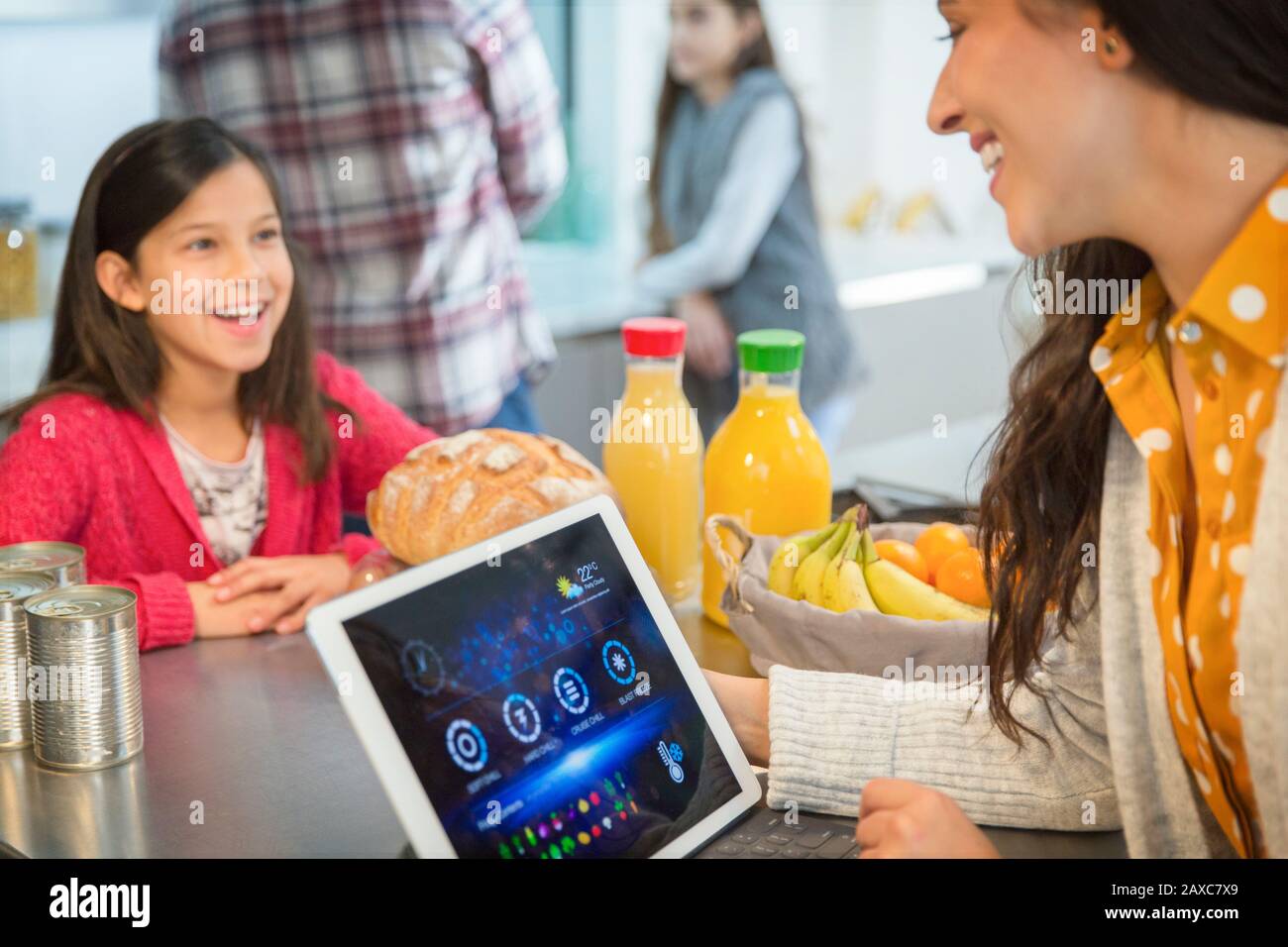 Madre e figlia che parlano, usando il tablet digitale in cucina Foto Stock