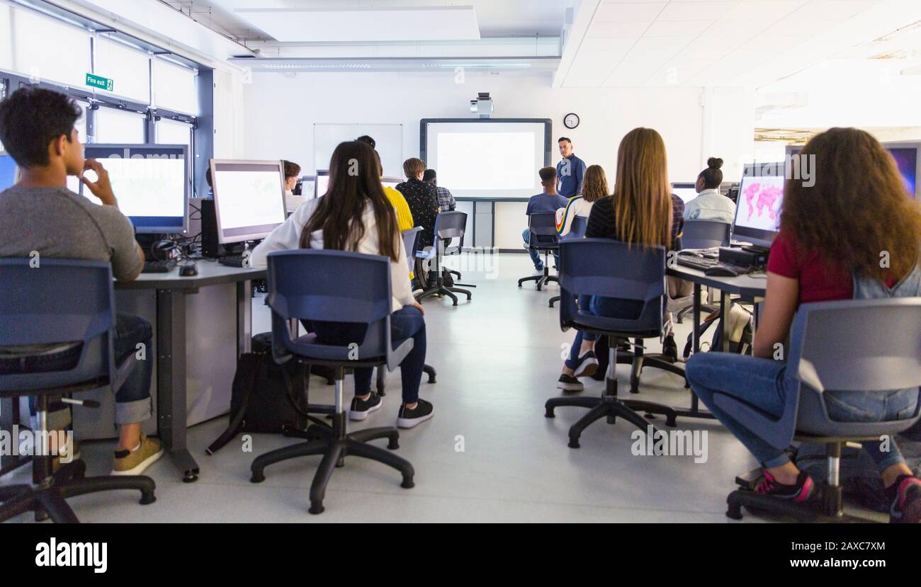 Giovani studenti di alto livello a computer che guardano l'insegnante a schermo di proiezione in classe Foto Stock