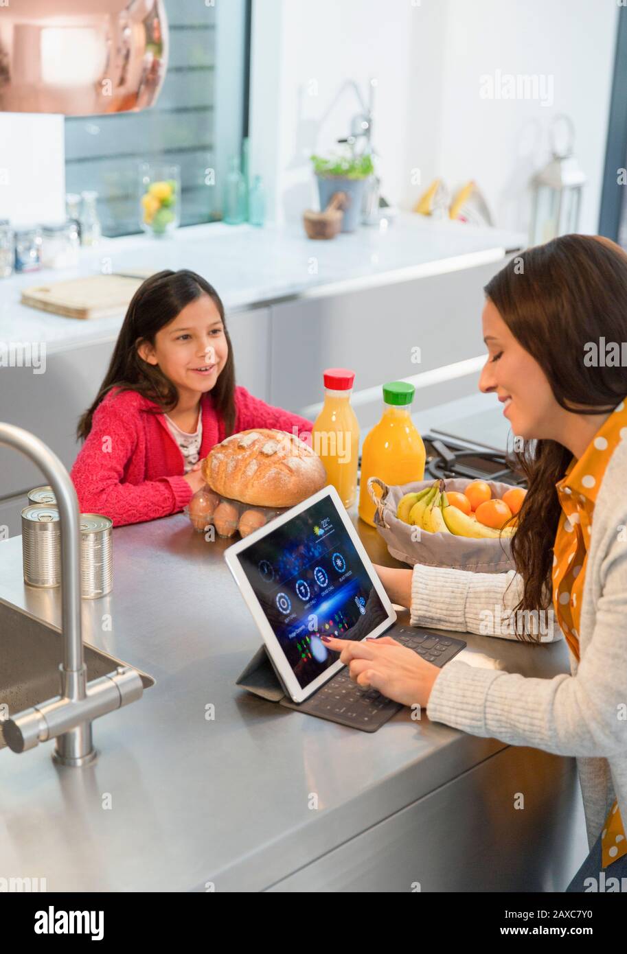 Figlia che guarda la madre utilizzando un tablet digitale in cucina Foto Stock