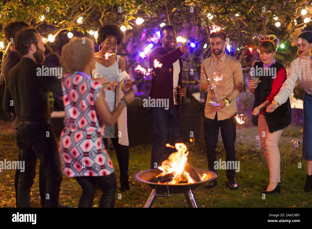 Amici con sparklers intorno alla buca del fuoco alla festa del giardino Foto Stock