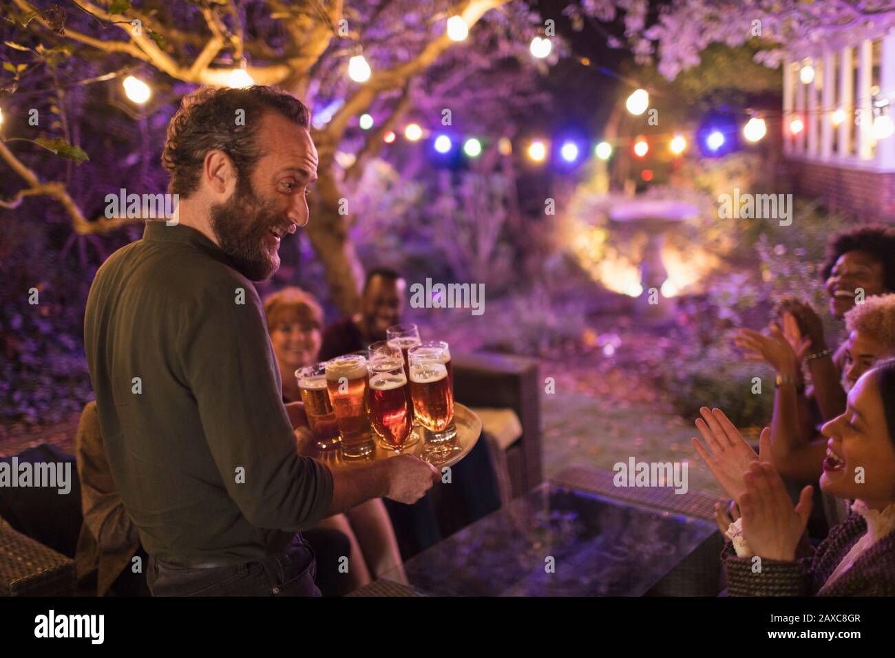 Uomo sorridente con vassoio di birre che serve gli amici a festa in giardino Foto Stock