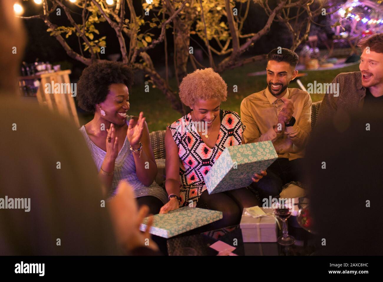 Amici che guardano donna aperto compleanno dono a festa giardino Foto Stock
