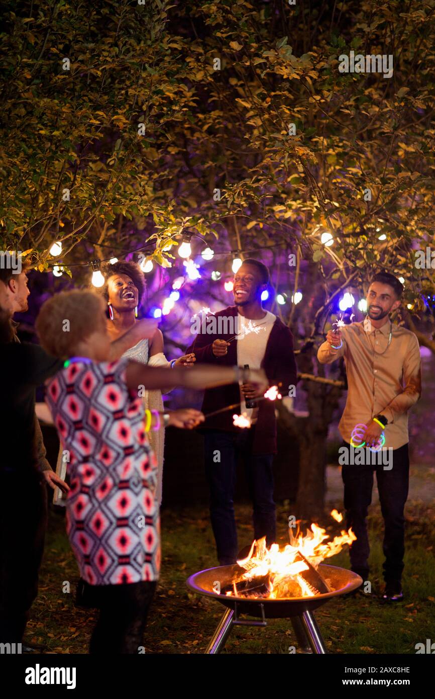 Amici felici con sparklers intorno al pozzo del fuoco alla festa del giardino Foto Stock
