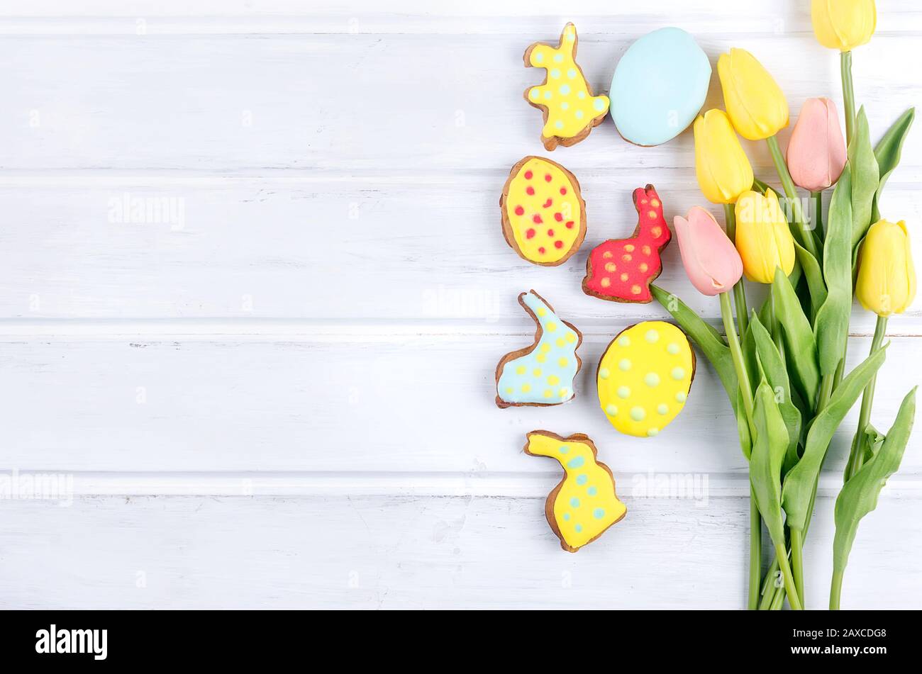 Tulipani gialli e biscotti di pan di zenzero di Pasqua su tavola di legno bianco. Concetto di vacanza primaverile o pasquale, spazio per le copie, disposizione piatta, messaggio di saluto "Template mockup" Foto Stock