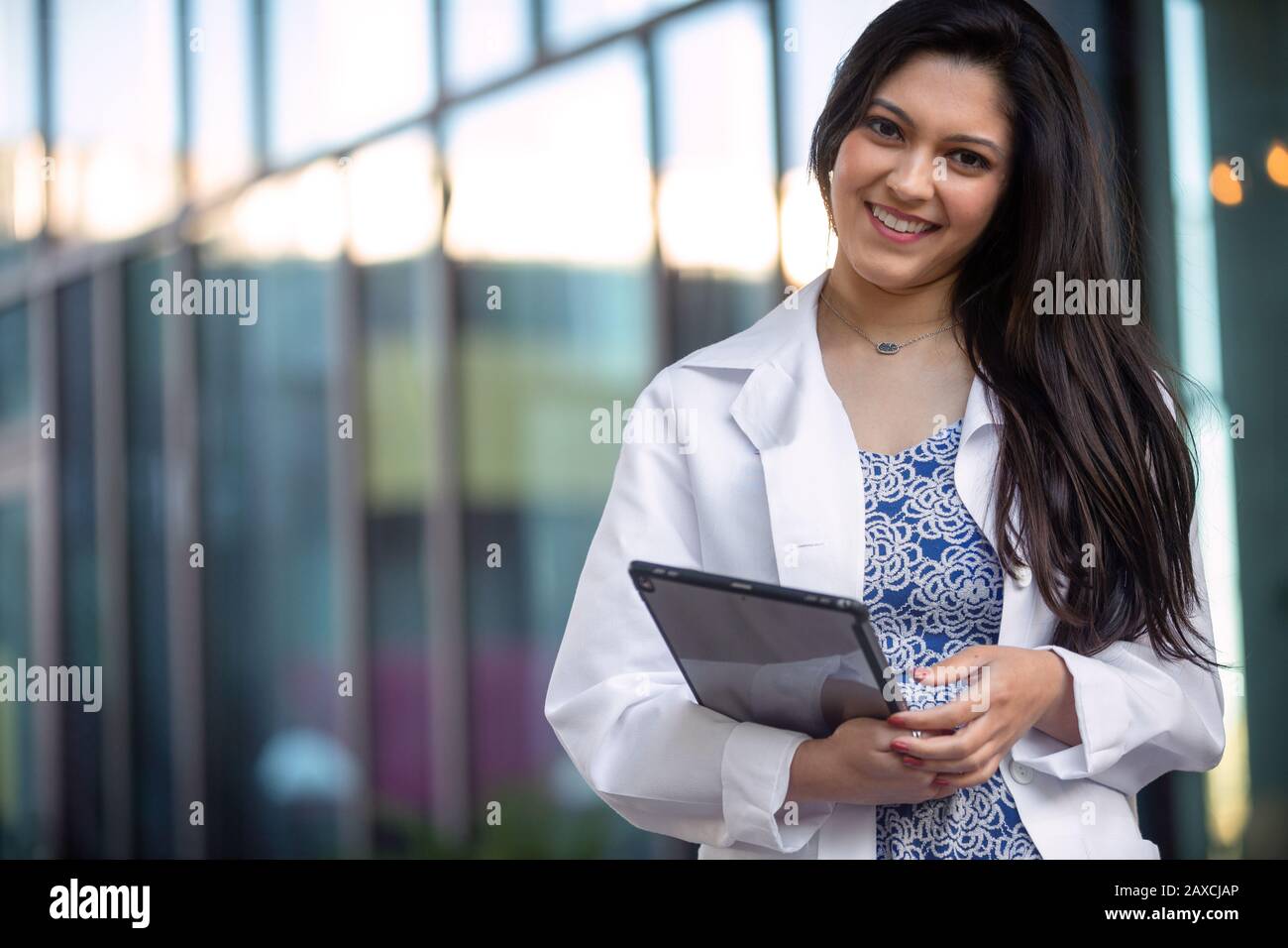 Bella donna indiana americana in un camice da laboratorio, veste bianca con tablet elettronico, medico professionista sorridente ritratto Foto Stock