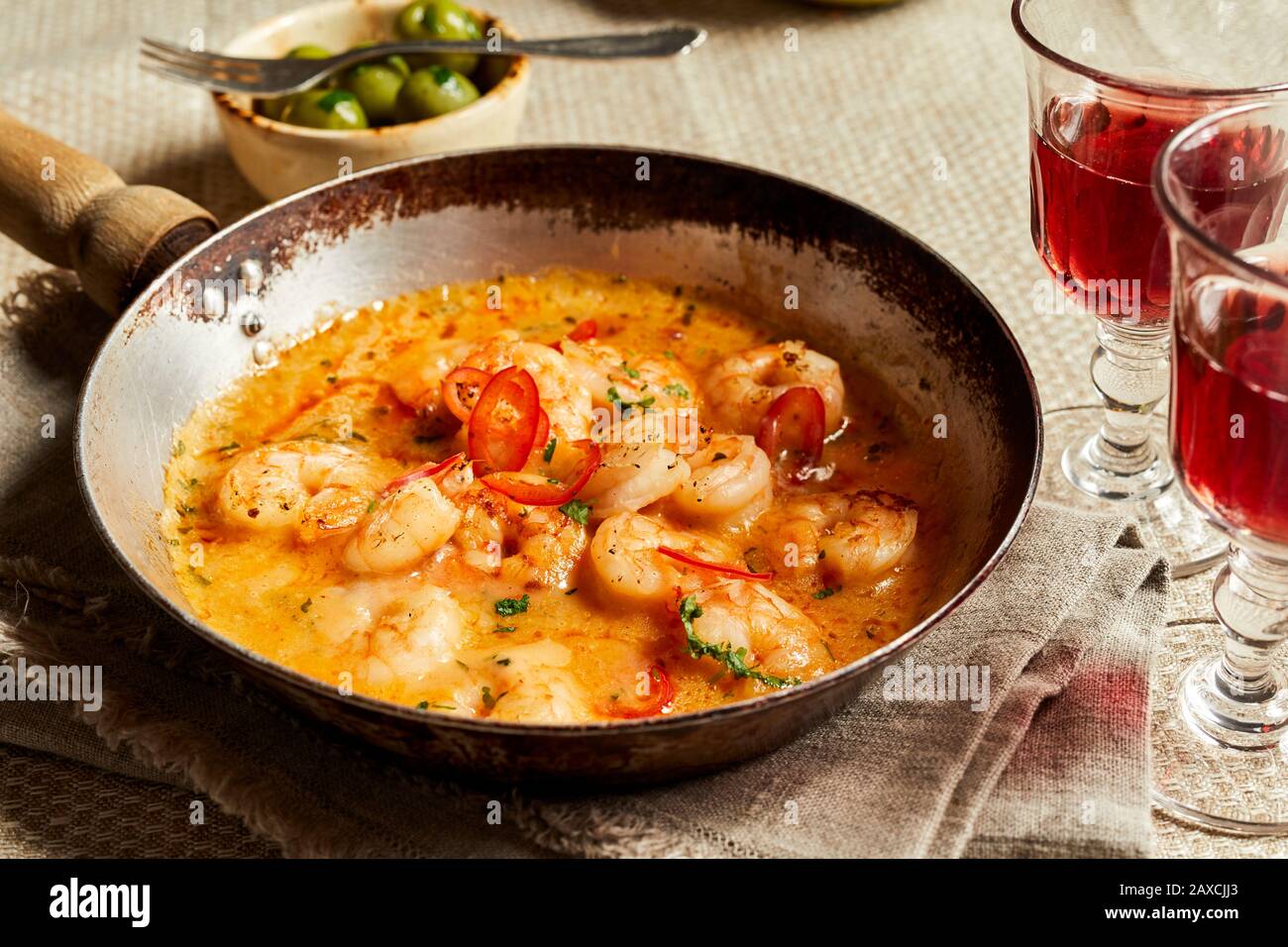 Servizio di peri scampi con due bicchieri di vino rosso servito in una vecchia padella con salsa cremosa al peperoncino ed erbe aromatiche Foto Stock