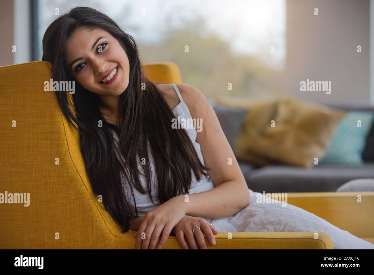 Caldo e cordiale ritratto sincero di una donna indiana di etnia mista, simpatica e genuina a casa, rilassante sul divano Foto Stock