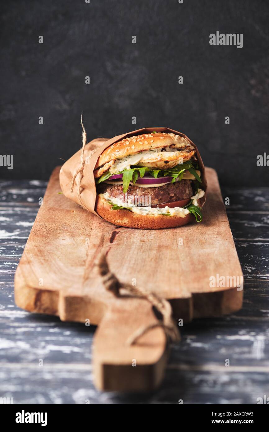Un grande hamburger appetitoso con tortino di manzo alla griglia e verdure fresche. Gustoso cheeseburger americano su una tavola di legno. Hamburger classico fatto in casa Foto Stock