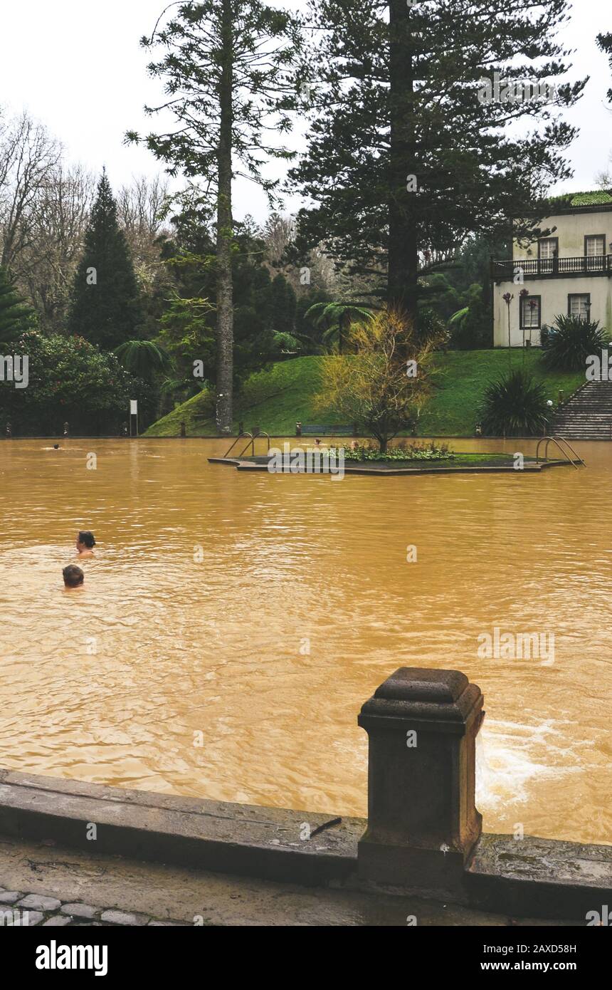 Furnas, Azzorre, Portogallo - 13 gennaio 2020: Piscina termale con acqua calda di ferro nel Giardino Terra nostra. Persone che nuotano in acqua di colore marrone da una sorgente vulcanica. Attrazione turistica portoghese. Foto Stock