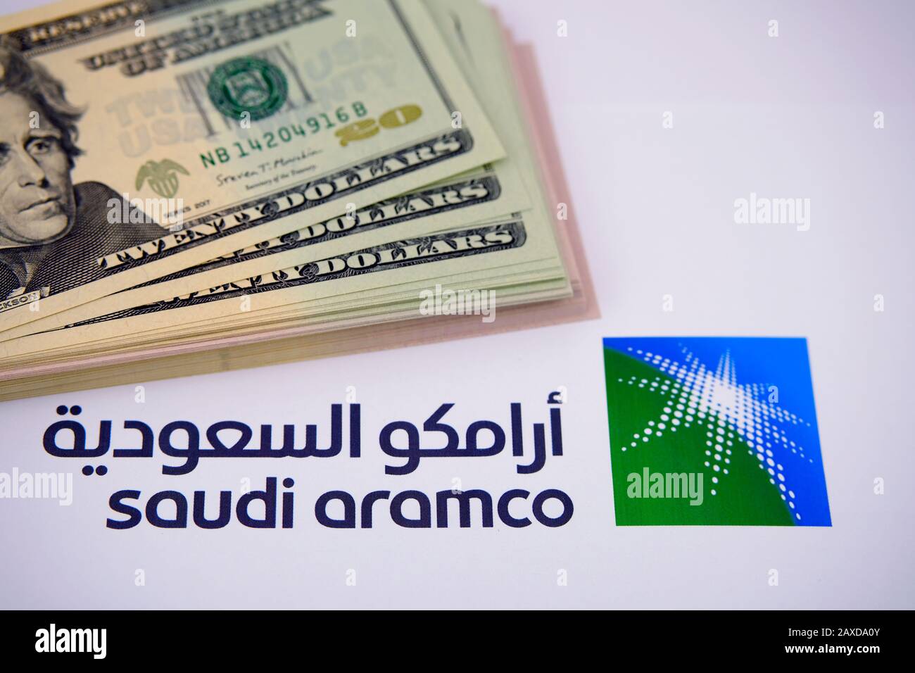 Il logo Saudi Aramco e la pila di banconote in dollari. Saudi Arabian Oil Company è una delle più grandi aziende del mondo per entrate. Foto Stock