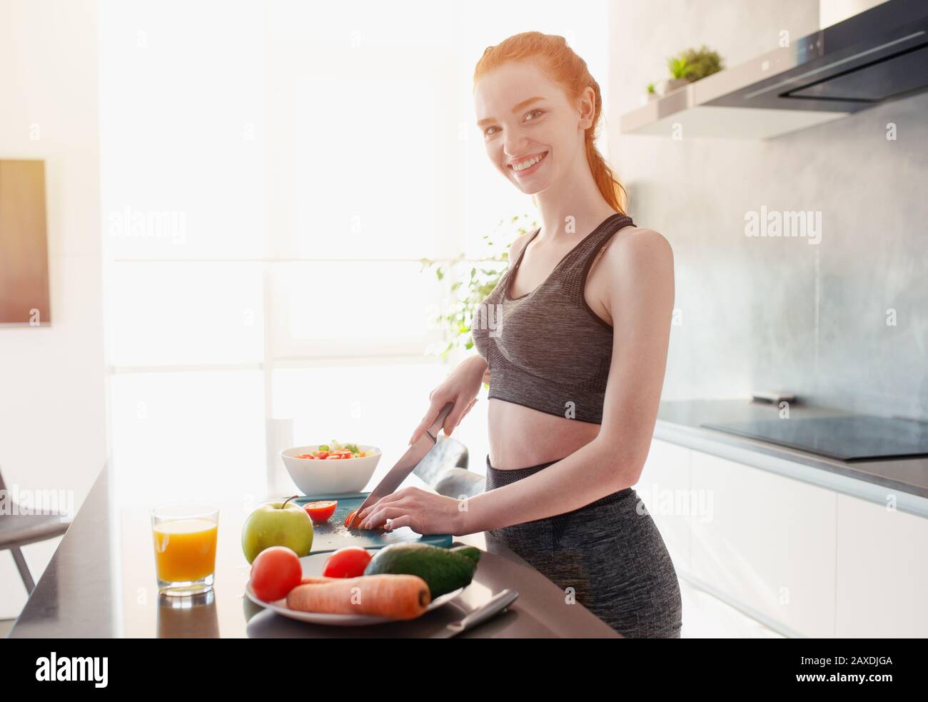 Ragazza atletica con abiti da palestra mangia frutta in cucina Foto Stock