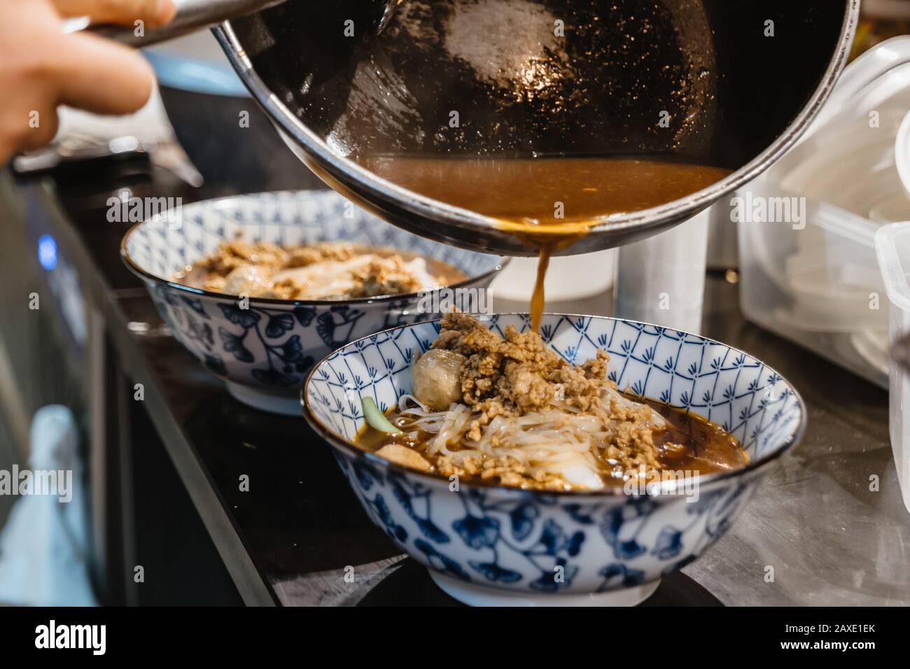 Versando zuppa di marrone di stile Thai con carne, maiale e palla di carne su spaghetti di riso e verdure in ciotola, al banco presso la cucina del ristorante. Foto Stock
