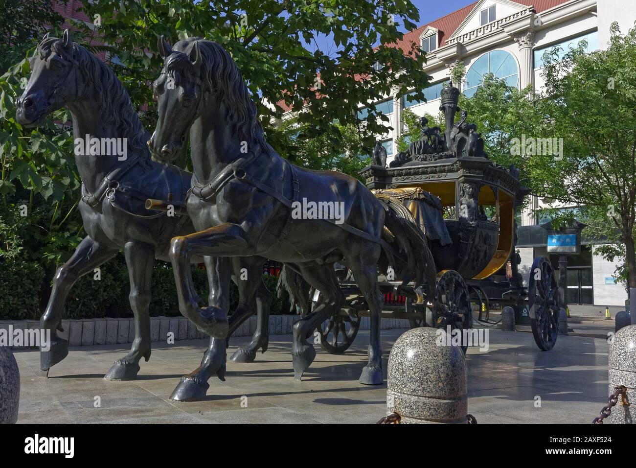 Grandangolo della statua di due cavalli che portano un carro in un parco circondato da alberi Foto Stock