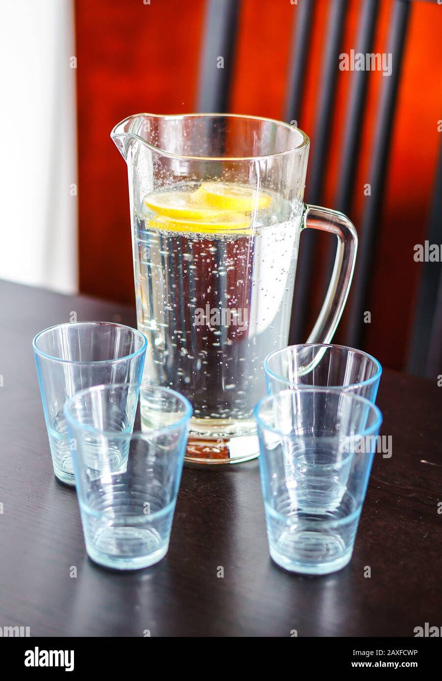 Decantatore d'acqua con fette di limone e acqua in esso il tavolo con gli occhiali Foto Stock