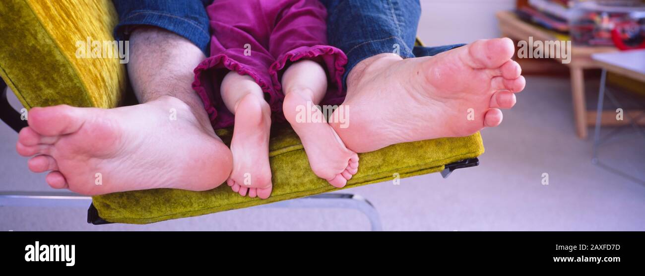 Primo piano dei piedi di un uomo e di sua figlia sdraiati su un divano Foto Stock