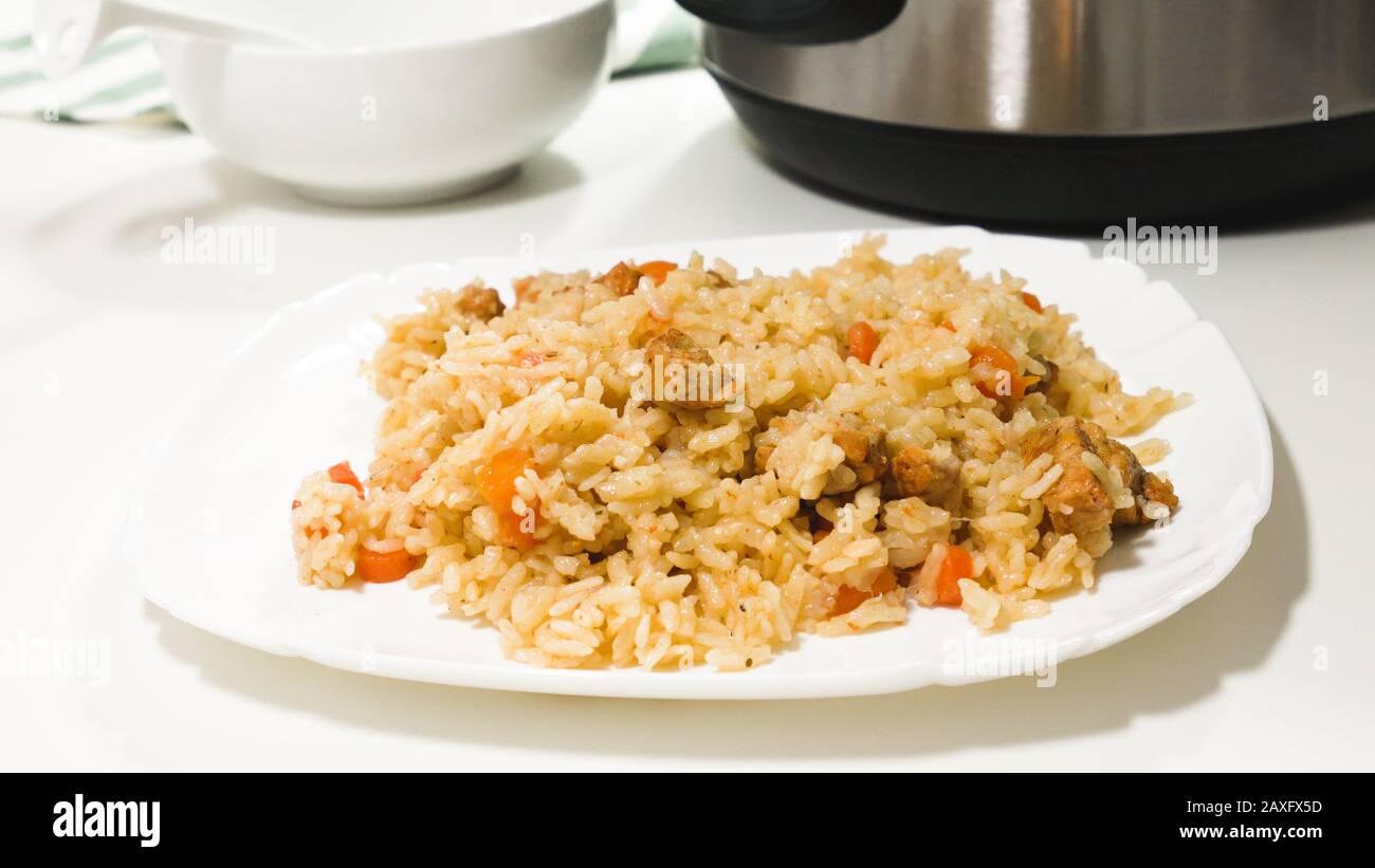 Riso con carne e verdure (riso Pilaf) cucinato in multicooker, primo piano su un piatto con fondo bianco Foto Stock