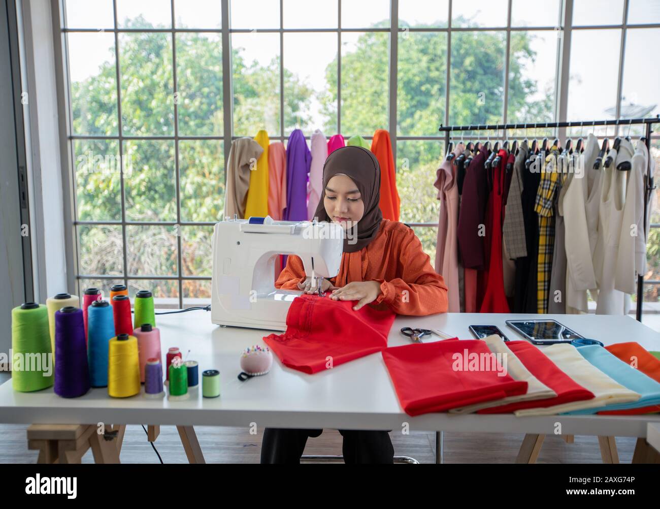 Piccola impresa di designer di moda donna musulmana Che Lavora e utilizza smartphone e tablet Con abiti al negozio di abbigliamento Foto Stock