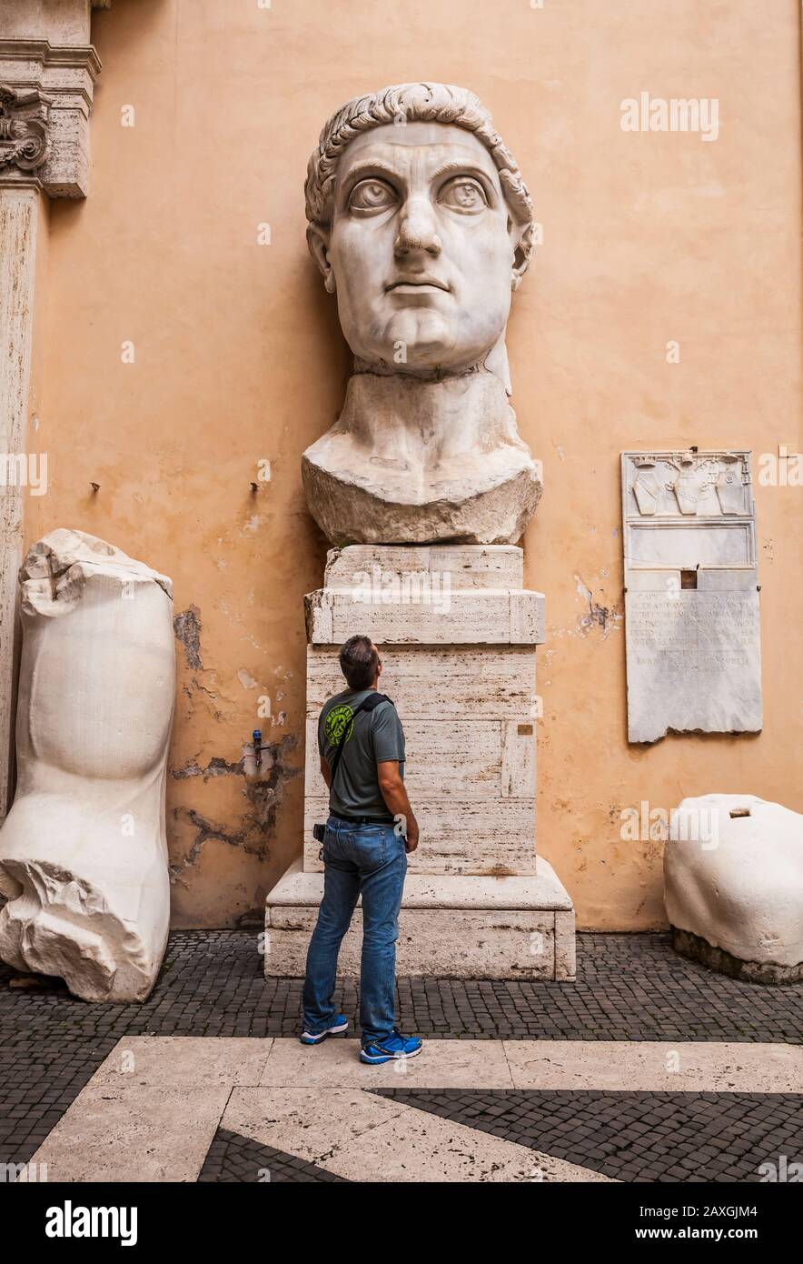 I frammenti e la testa della colossale statua di Costantino con un uomo che si trova sotto a guardarlo. Museo Capitolino, Roma Italia. Foto Stock