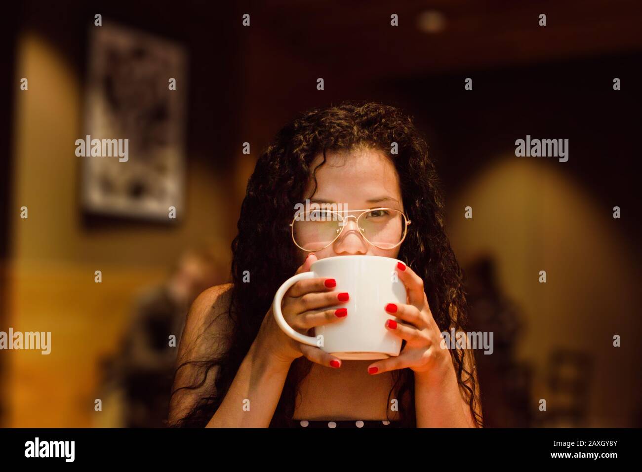 Donna latina che beve una tazza di caffè. Ritratto di bella ragazza afro-americana con occhiali su una caffetteria. Foto Stock