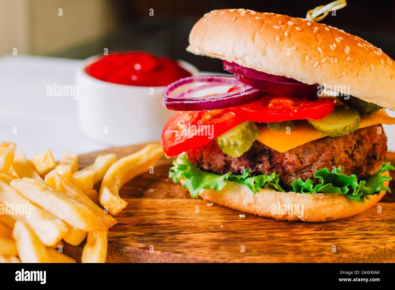 Primo piano di un burguer completo, con lettucce, cheader formaggio, sottaceti, pomodoro, cipolle e pane con semi di sesamo, su uno sfondo rustico Foto Stock