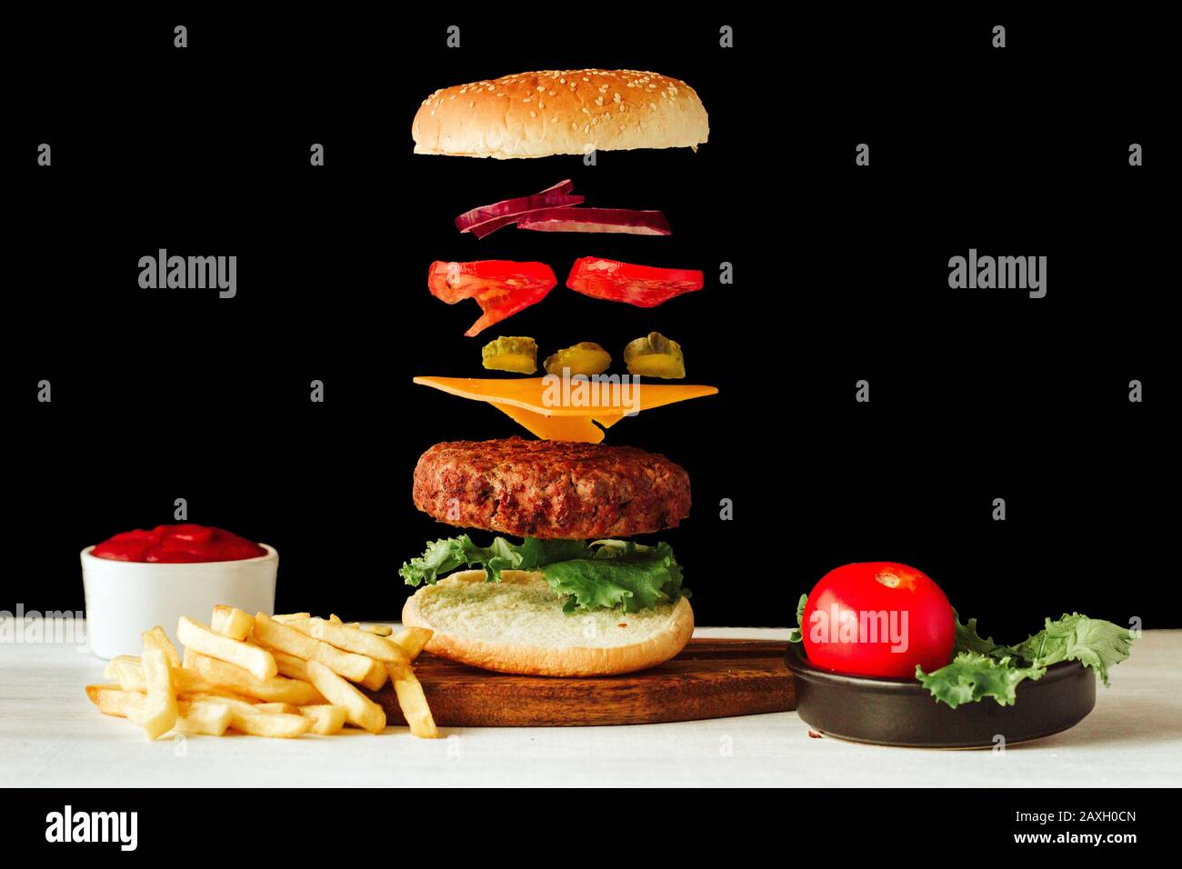 Hamburger di manzo galleggiante. Gustosa carne alla griglia con ingredienti di pesce volante su sfondo bianco e nero con ketchup e patatine fritte fatte in casa Foto Stock