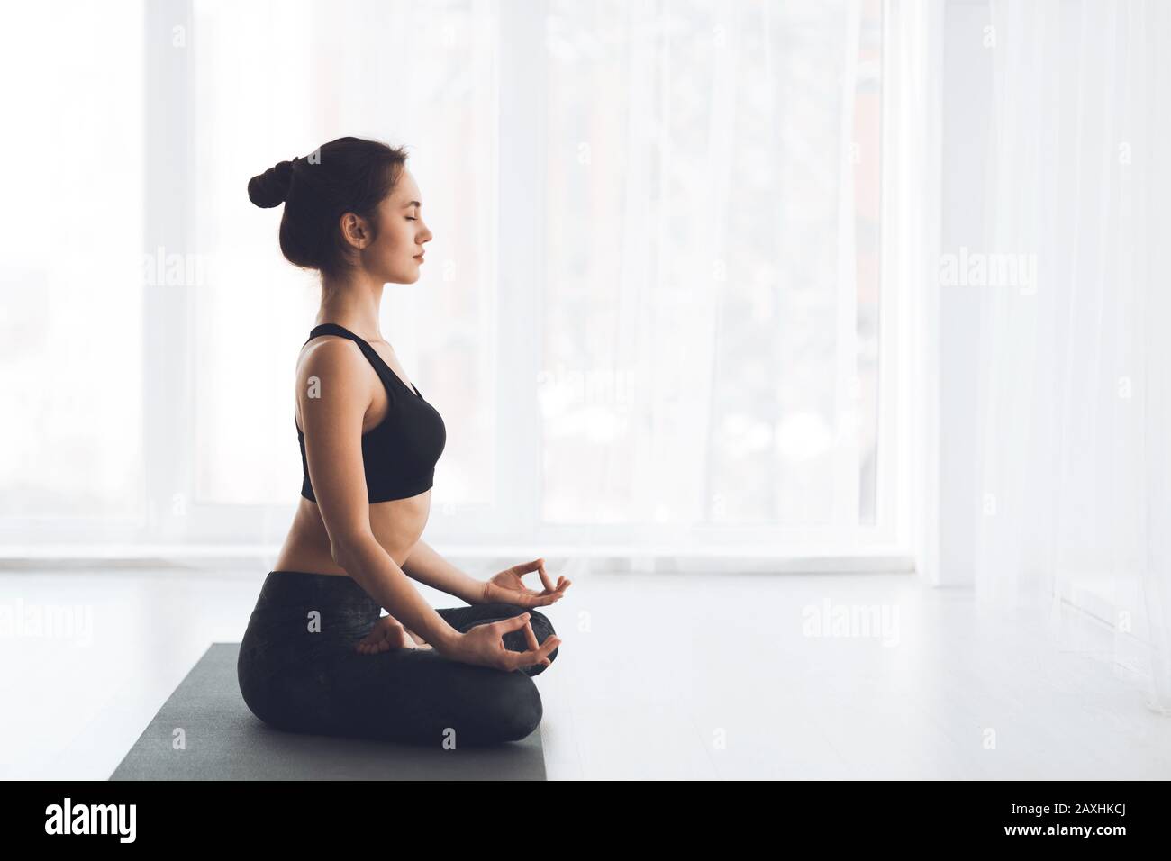 Vista laterale della ragazza sottile che pratica yoga seduto sul tappetino Foto Stock