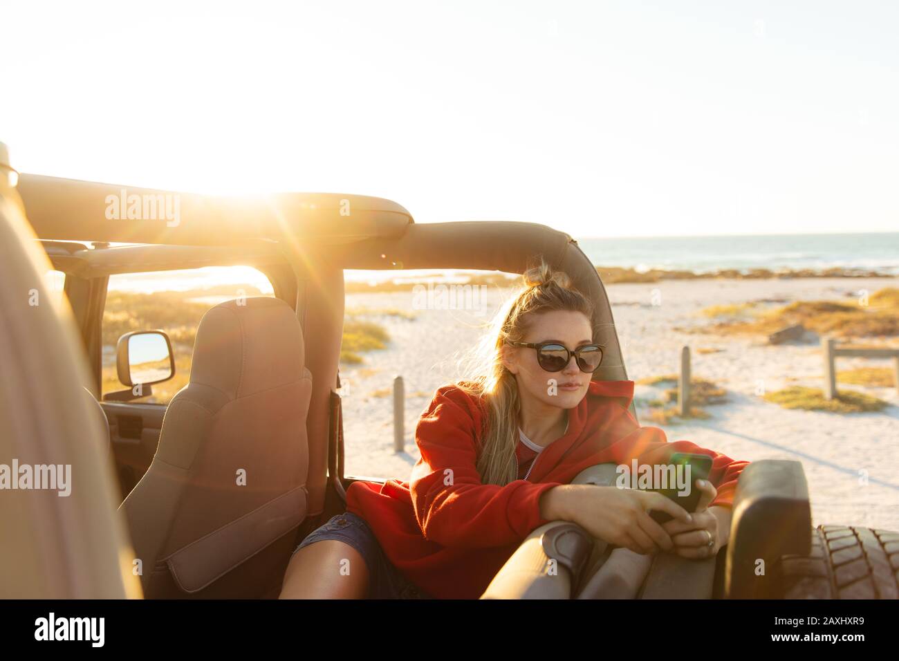 Vista frontale di una donna caucasica all'interno di un'auto a cielo aperto, che si affaccia durante il tramonto. Weekend vacanza in spiaggia, stile di vita e tempo libero. Foto Stock