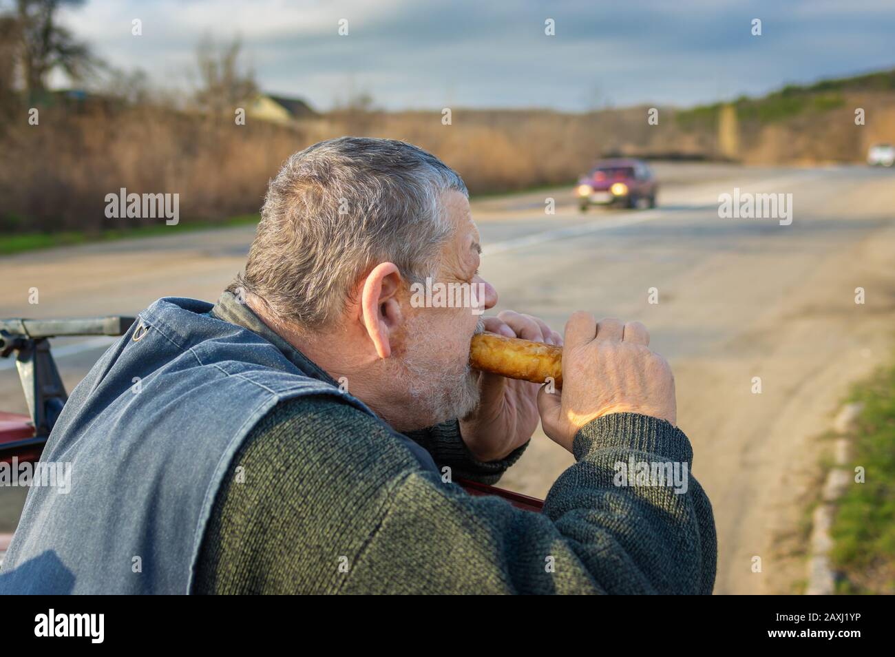 Ritratto del pilota caucasico affamato che nibbling patty appoggiato i gomiti sulla porta dell'auto Foto Stock