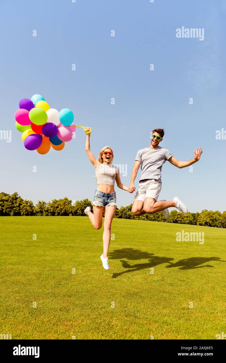 Uomo e donna felici che tengono palloncini e saltano nel parco Foto Stock
