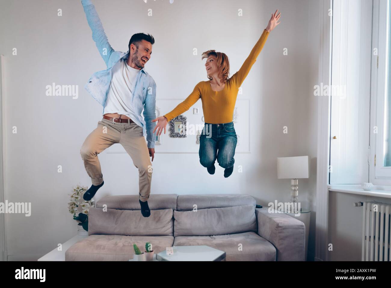 Felice coppia innamorata divertirsi insieme saltando sul divano nel soggiorno a casa. Concetto di attività per il tempo libero Foto Stock