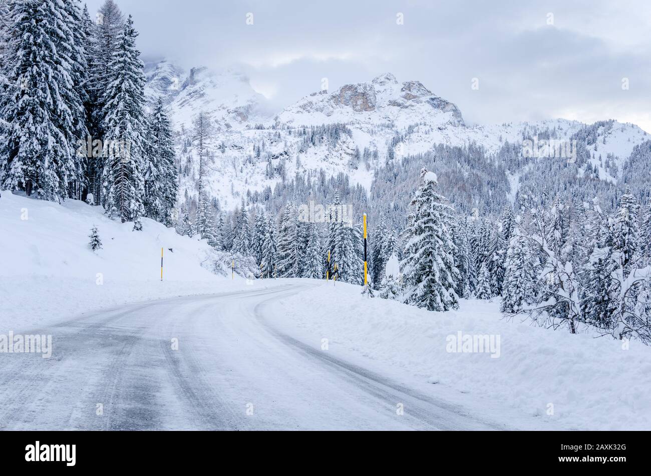Neve tortuosa strada di montagna ai piedi delle cime torreggianti delle Dolomiti in una torbida giornata invernale Foto Stock