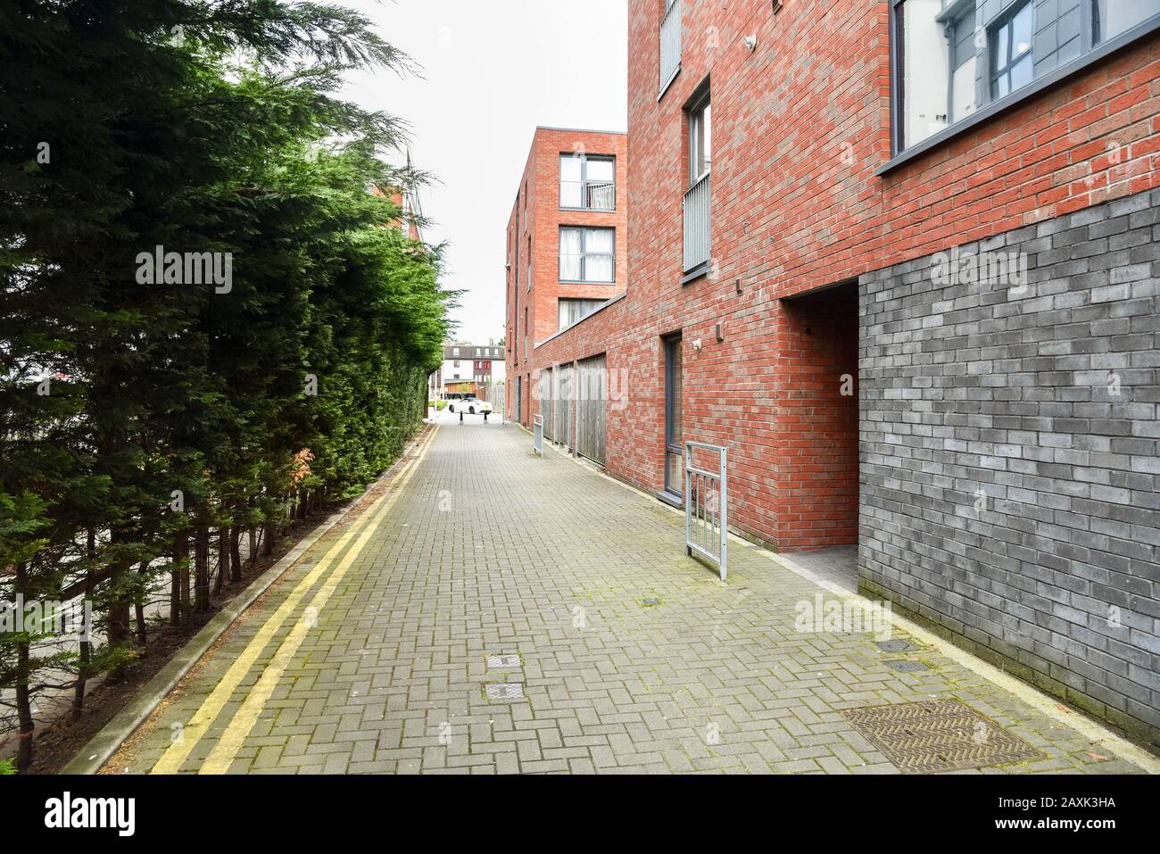 Strada pedonale lastricata deserta che corre lungo un moderno edificio di appartamenti in mattoni Foto Stock