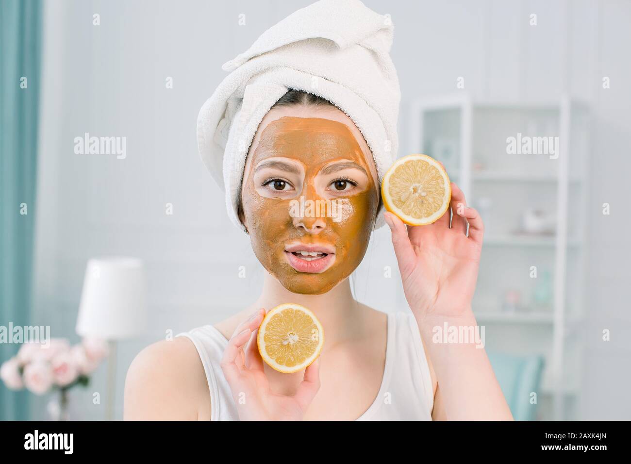 Bella ragazza con maschera facciale marrone che tiene una fetta di limone  vicino al suo viso