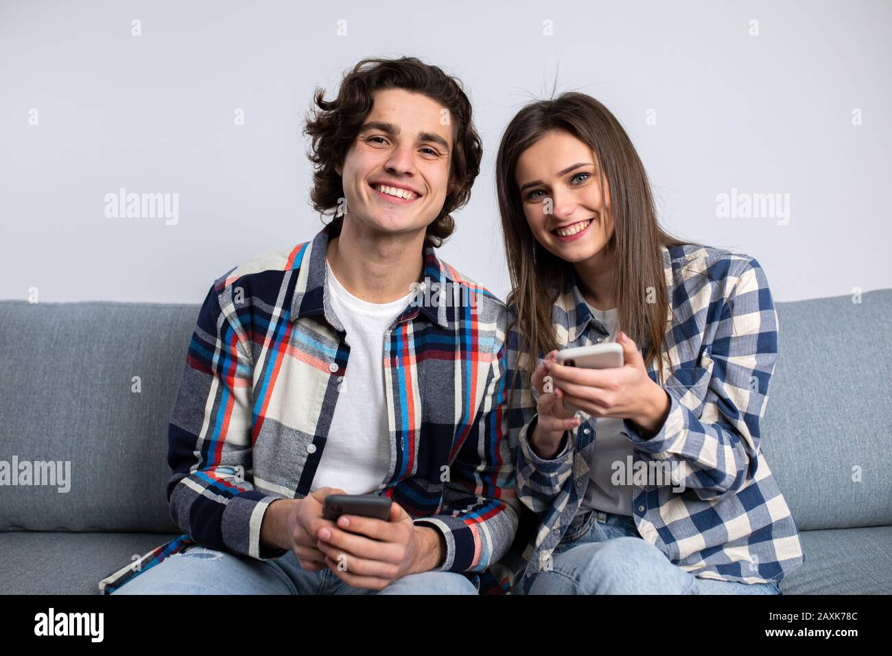 Felice coppia utilizzando gli smartphone con sorriso in salotto. Foto Stock Felice coppia utilizzando gli smartphone con sorriso in salotto. Foto Stock