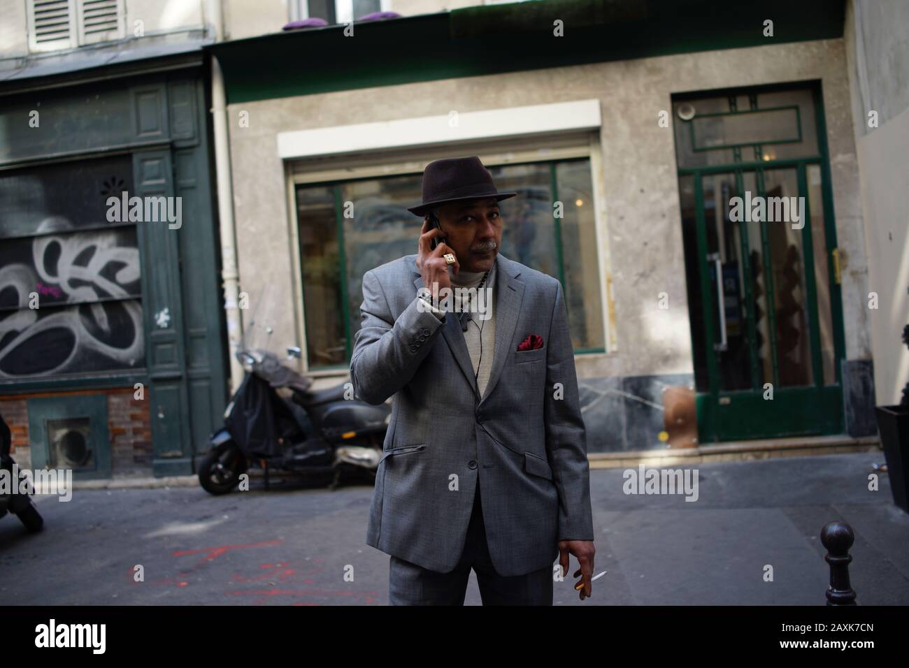 Uomo in abito grigio e cappello che tiene il telefono cellulare per l'orecchio, fumare - foto di strada Foto Stock