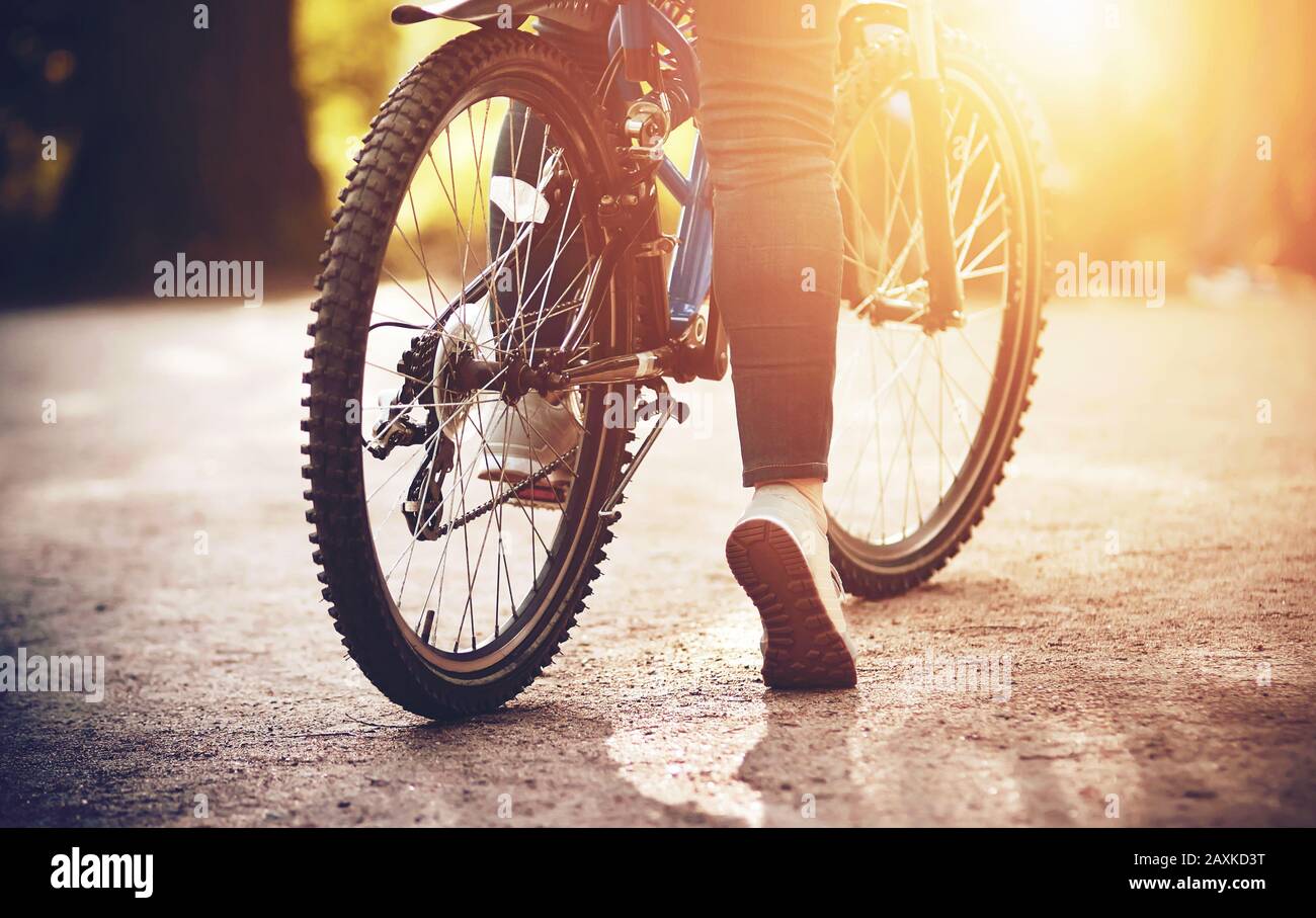 Una bicicletta sportiva a velocità su cui una ragazza è seduta nel mezzo di un percorso Park è illuminata dalla luce brillante del sole estivo. Sport ricreazione Foto Stock