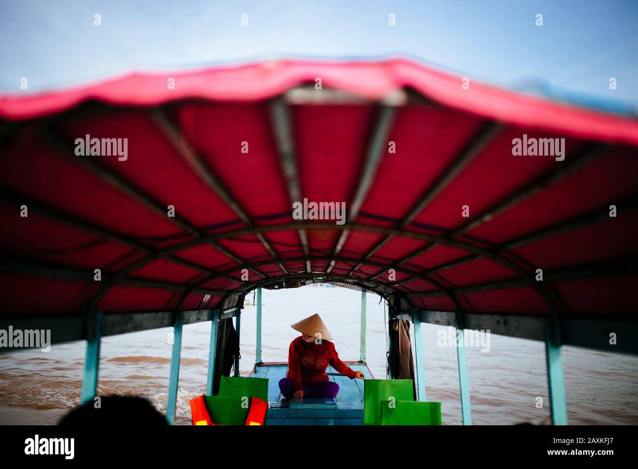 Donna che pilota una barca con baldacchino rosso attraverso un fiume. Foto Stock
