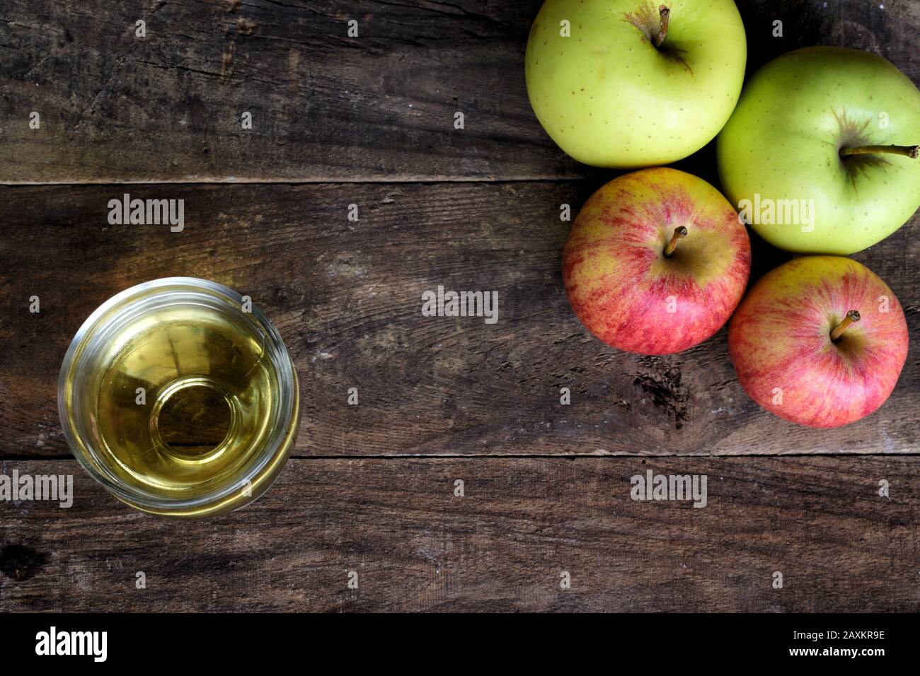 Un bicchiere di succo di mela trasparente accanto a un mazzo di mele sulla parte superiore di un vecchio tavolo di legno Foto Stock
