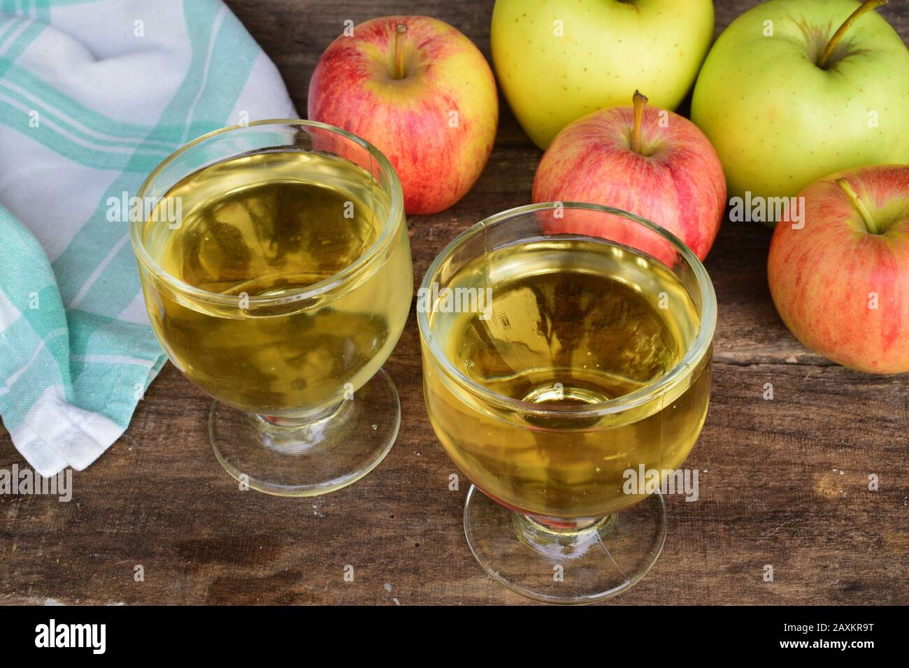 Due bicchieri con succo di mela fresco chiaro e alcune mele sul lato e una tovaglia sul lato su un vecchio tavolo di legno Foto Stock