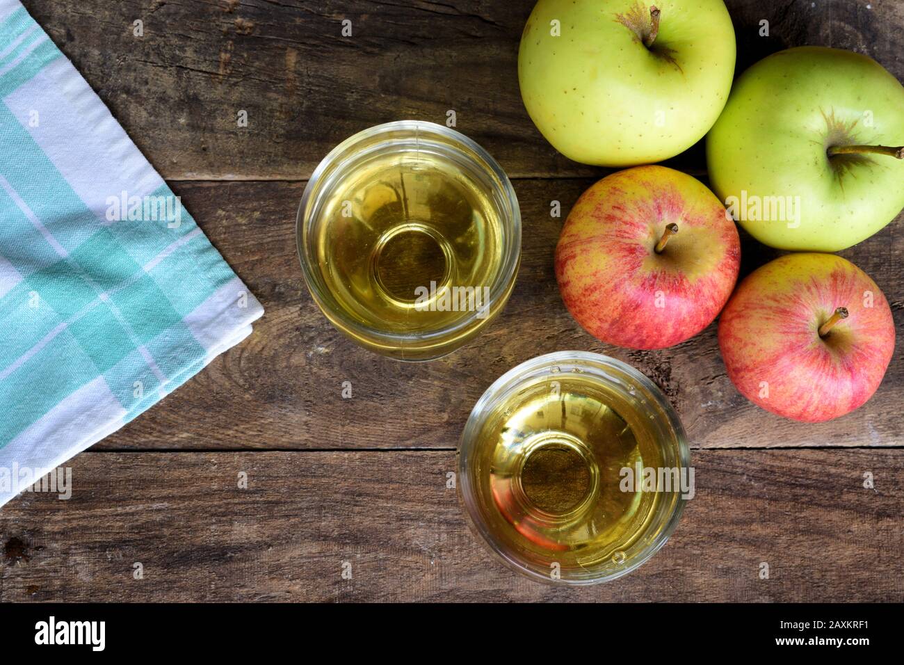 Un mazzo di mele con due bicchieri con succo di mela sopra un vecchio tavolo di legno e un panno da tavolo verde e bianco Foto Stock