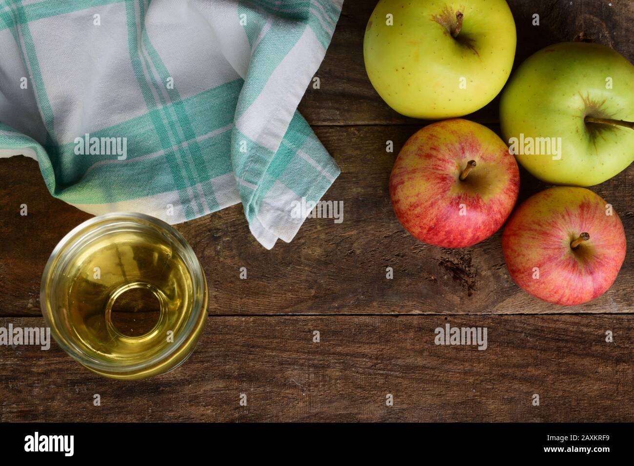 Succo di mela e alcune mele sulla parte superiore di un vecchio tavolo di legno con una tovaglia verde e bianca su un lato Foto Stock