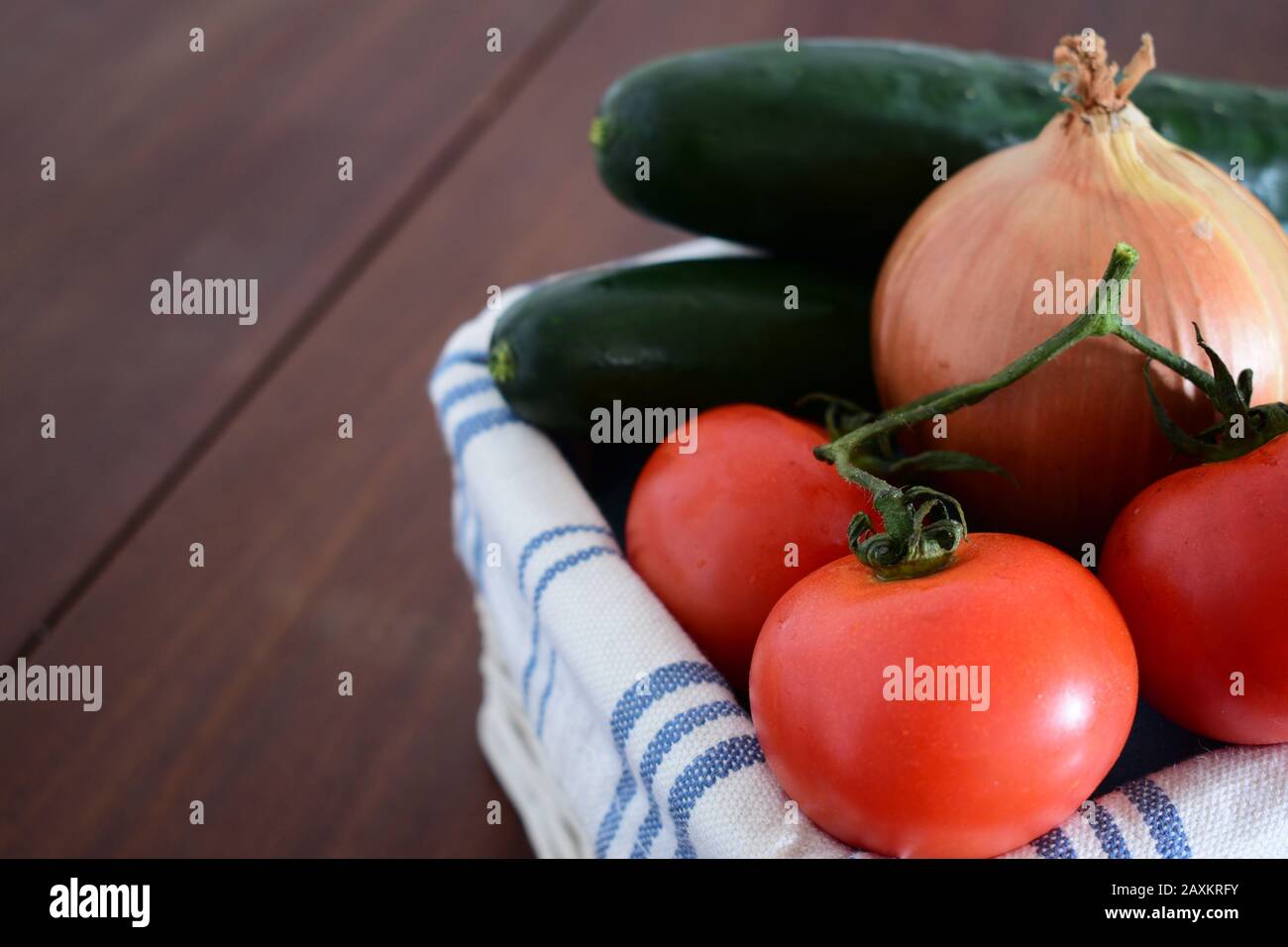 Un mazzetto di pomodori in un cesto con cetrioli sfocati e una cipolla sullo sfondo Foto Stock