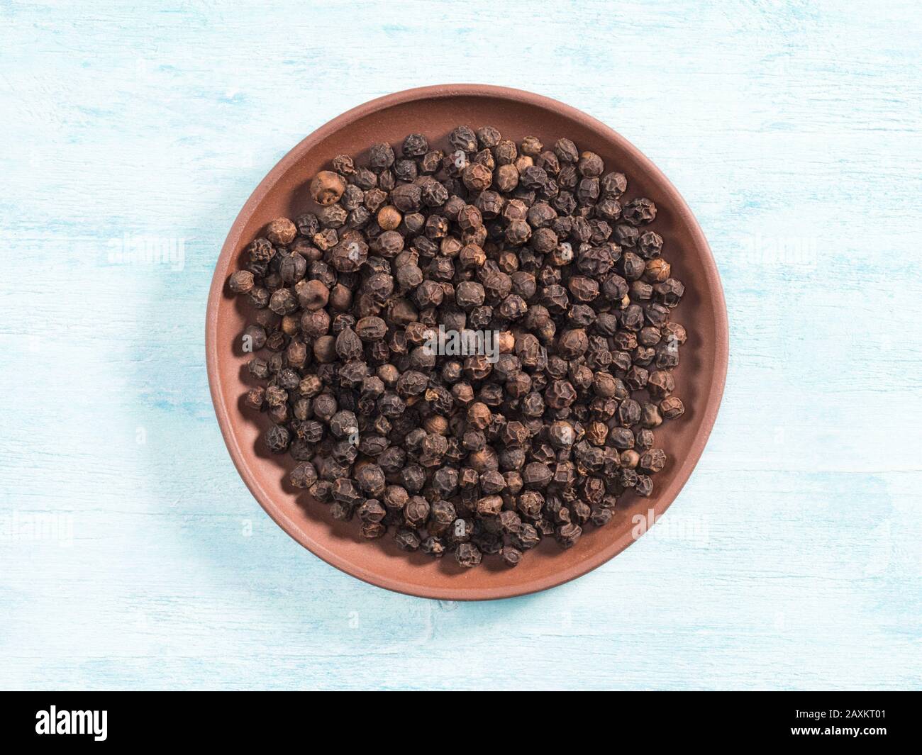 Pepe nero speziato in piastra di argilla su sfondo di legno blu Foto Stock