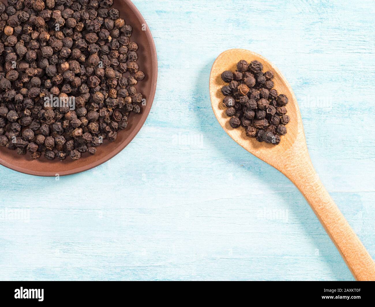Pepe nero speziato in piastra di argilla e cucchiaio di legno su sfondo di legno blu Foto Stock