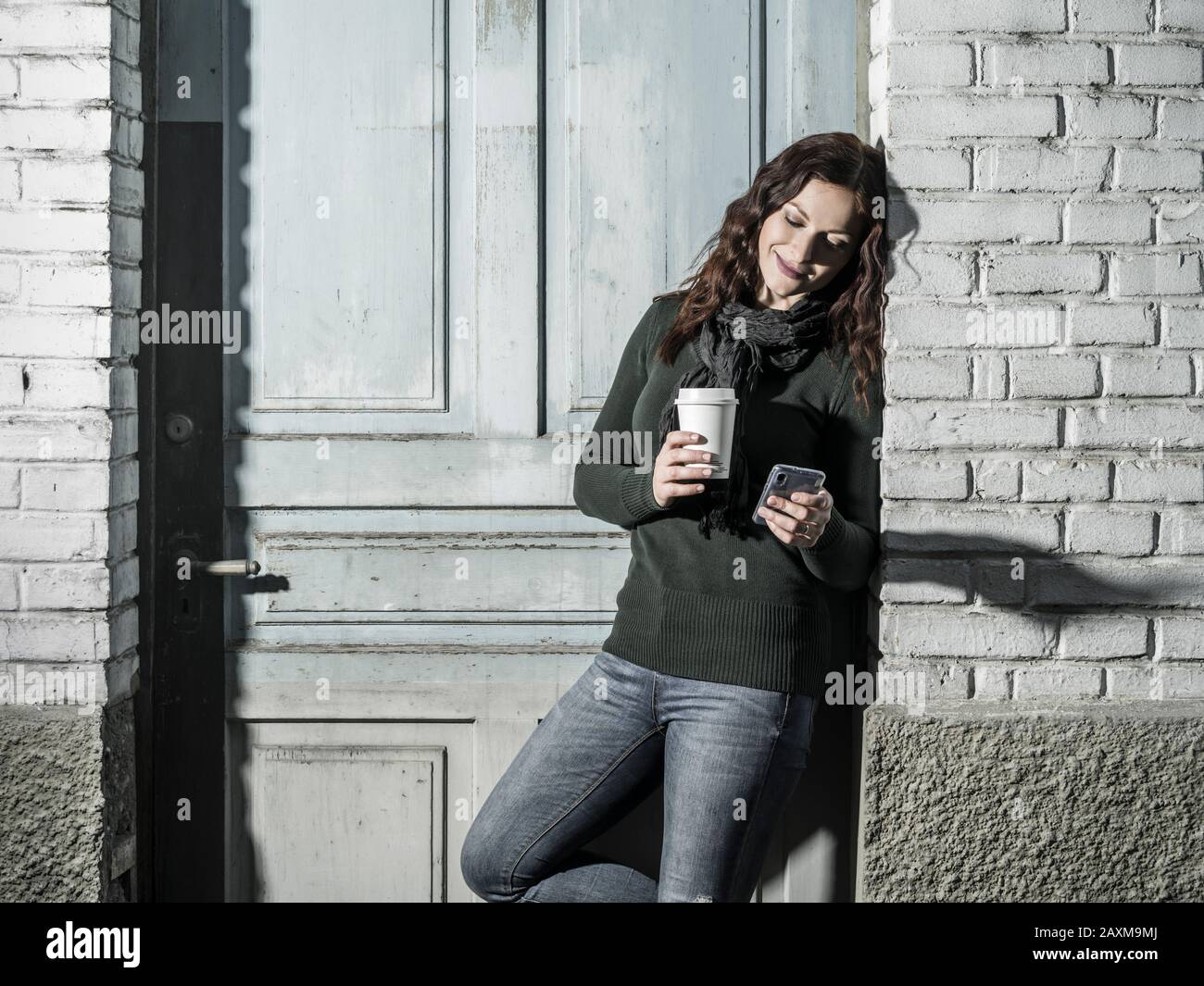 Giovane donna con i capelli rossi utilizzando il suo cellulare e di bere il caffè da una tazza di asporto. Foto Stock