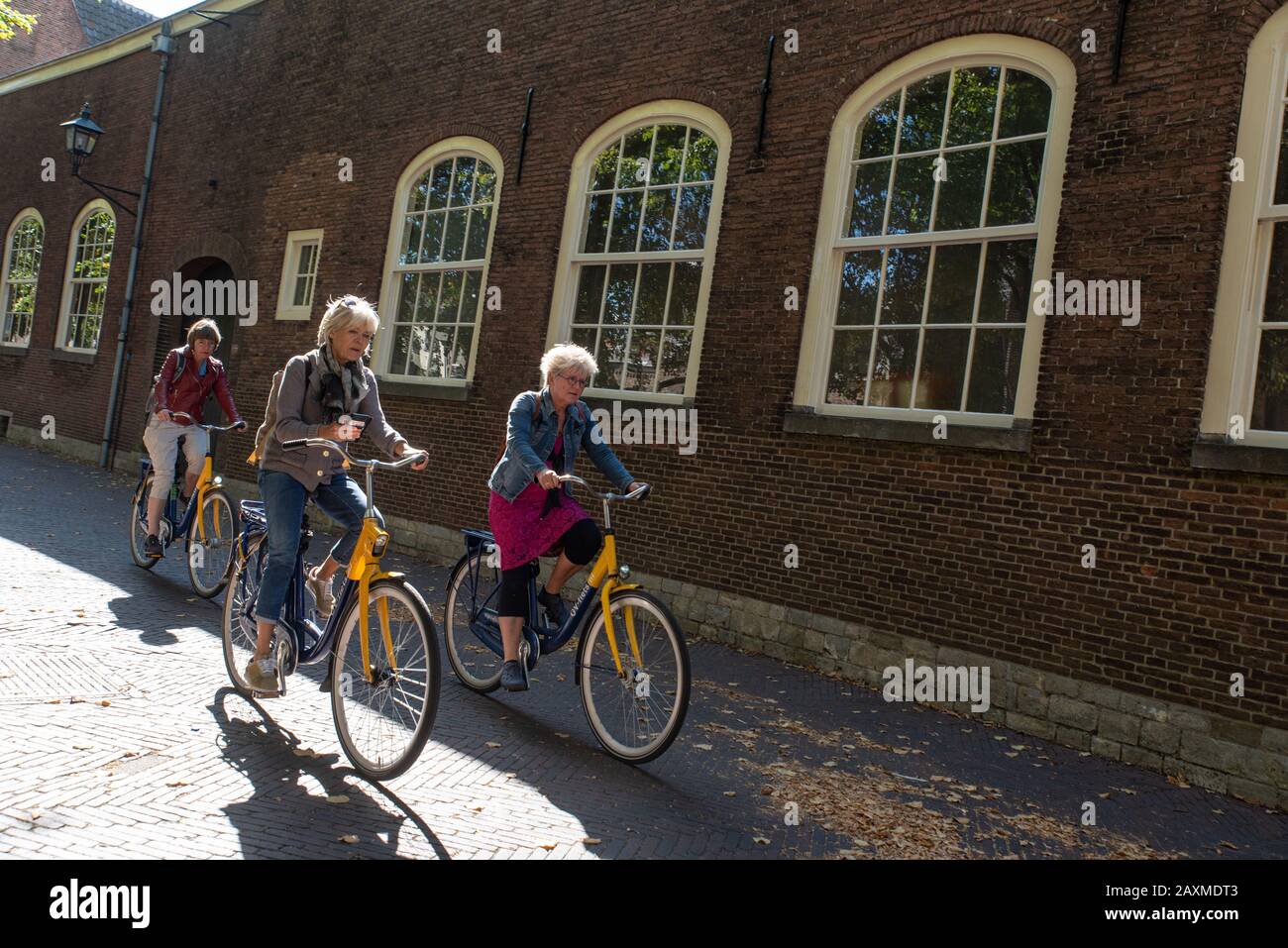 3 weibliche Touristen mittleren Alters, die durch die Straßen von Delft, die Niederlande radeln. // 3 turisti di mezza età che vanno in bicicletta attraverso il Foto Stock