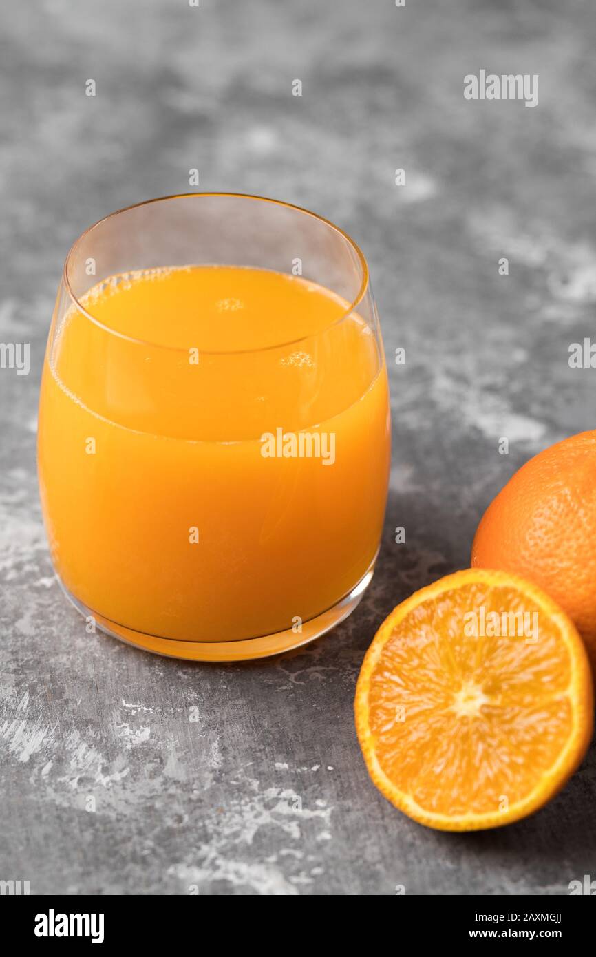 Un primo piano di succo d'arancia spremuto in un bicchiere trasparente su sfondo grigio Foto Stock