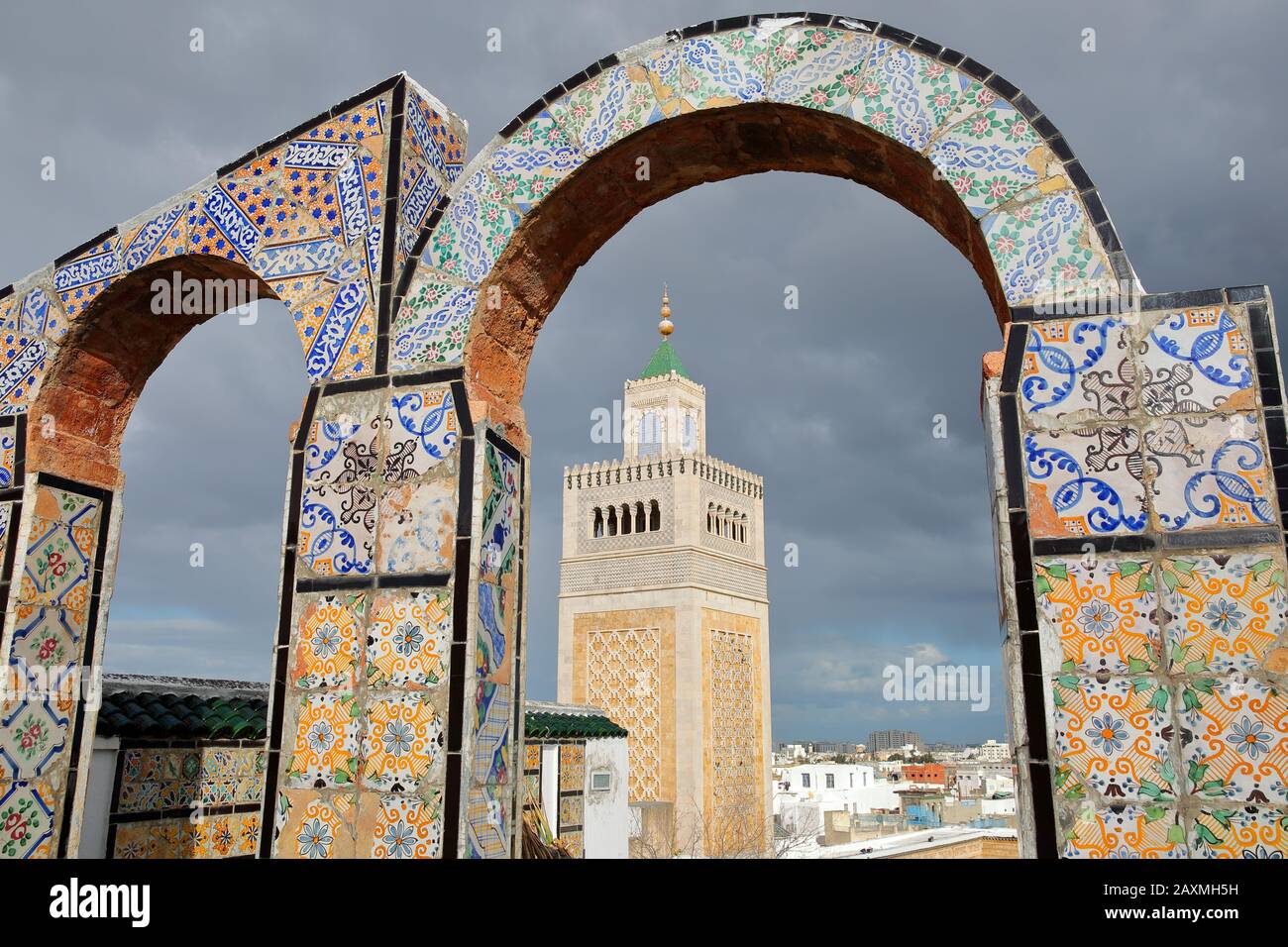 Vista sul minareto della Moschea Di Ez Zitouna (Grande Moschea) attraverso archi piastrellati colorati, situato su un tetto che si affaccia sulla medina di Tunisi, Tunisia Foto Stock
