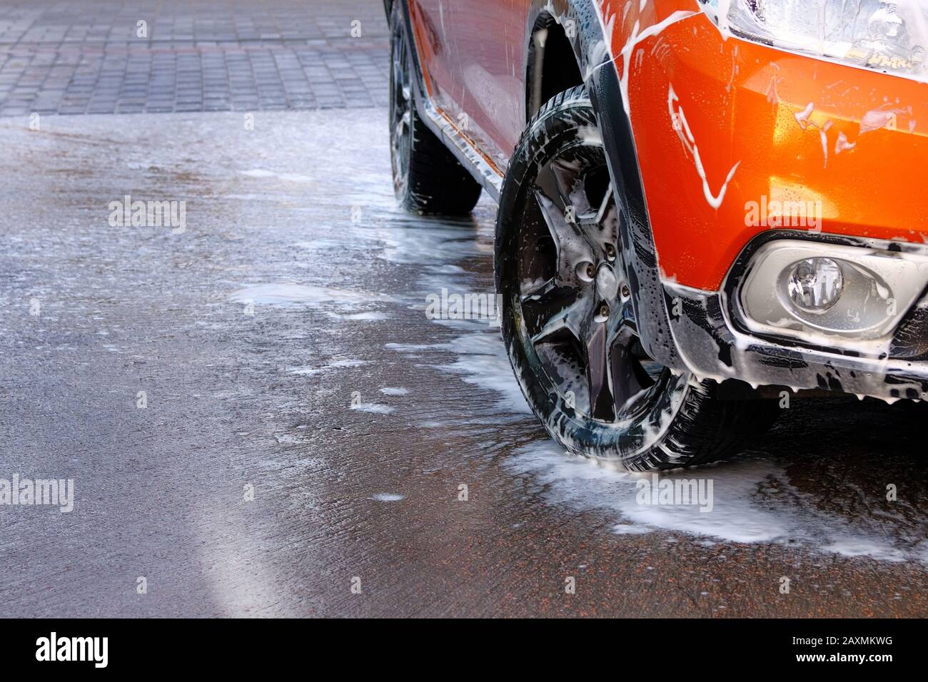 Chiusura ruote auto. L'automobile sta pulendo con i suds del sapone all'autolavaggio di self-service. Acqua saponata bianca. Foto Stock